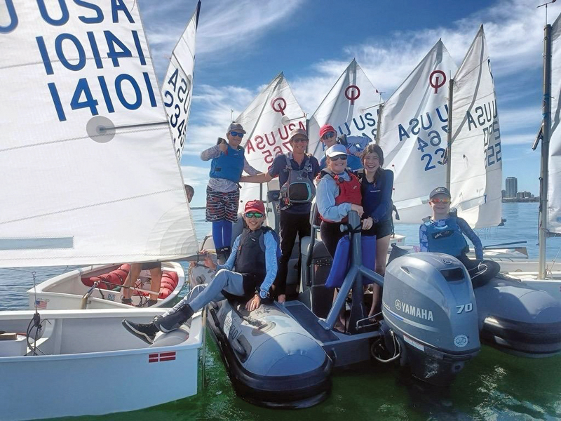 Youth sailing coach and young sailors on the water.